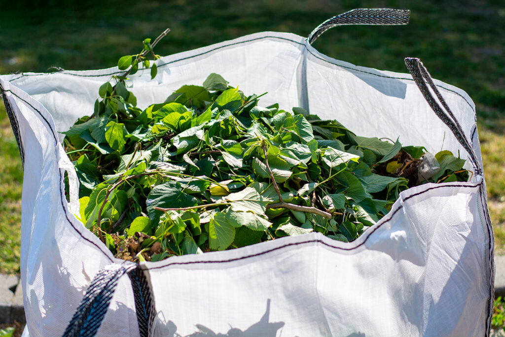 Ein großer Sack voller frischer Gartenabfälle, hauptsächlich grüne Blätter und Zweige.