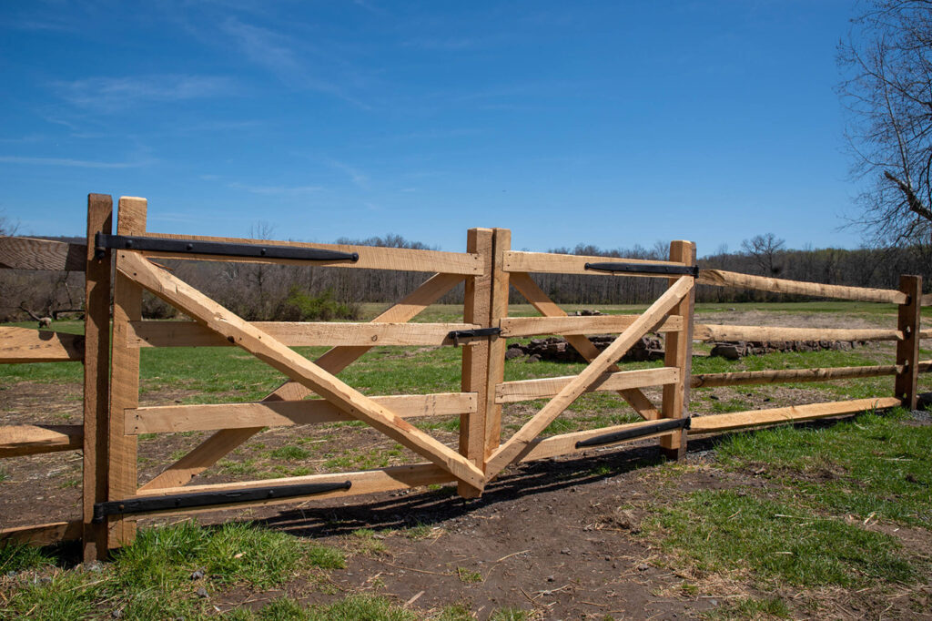 Weidezaunbau Holztor mit schwarzem Riegel in einer ländlichen Umgebung an einem sonnigen Tag.