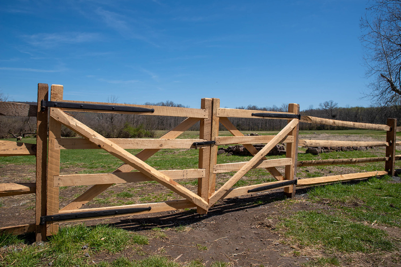 Holztor mit schwarzem Riegel in einer ländlichen Umgebung an einem sonnigen Tag.