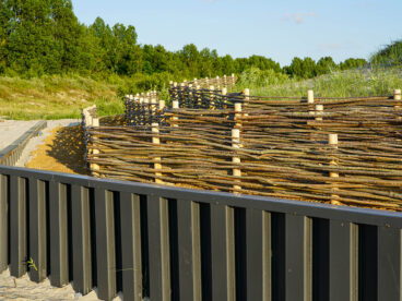 Ein innovativer Zaun aus Ästen und Holzpfosten in einer natürlichen Umgebung am Strand.